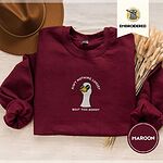 Maroon crewneck sweatshirt with a brown felt hat and dried bunny tail grass, embroidered with a cool white goose in black sunglasses with arched white lettering embroidered on the chest