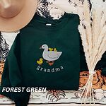 Forest Green crewneck sweatshirt folded with a tan felt hat and pampas grass, embroidered with a white mama duck, yellow ducklings and the word grandma in white thread