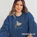 Woman wearing an Indigo Blue crewneck sweatshirt embroidered with a white mama duck, yellow ducklings and the word grandma in white thread