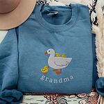 Indigo Blue crewneck sweatshirt folded with a tan felt hat and pampas grass, embroidered with a white mama duck, yellow ducklings and the word grandma in white thread