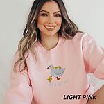 Woman wearing a Light Pink crewneck sweatshirt embroidered with a white mama duck, yellow ducklings and the word grandma in white thread