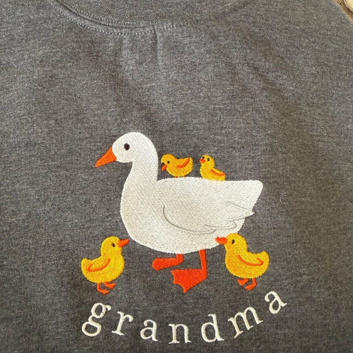Grandma Duck Sweatshirt with Four Ducklings Real Dark Heather grandma duck sweatshirt with four yellow ducklings, two on the mama duck's back and two at her feet, above the word grandma in white thread