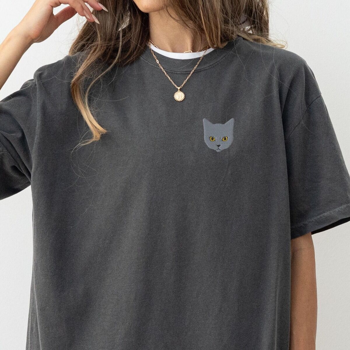 Grey Cat Shirt – Pepper Woman with a gold necklace in a Pepper T-shirt with a gray cat face with gold eyes embroidered on the left chest
