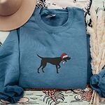 Indigo Blue crewneck sweatshirt laid flat with a tan hat and dried pampas grass, embroidered with a black German shorthaired pointer silhouette in a red Santa hat