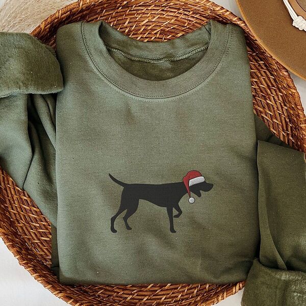 Military Green crewneck sweatshirt folded in a wicker basket, embroidered with a black German shorthaired pointer silhouette in a red Santa hat