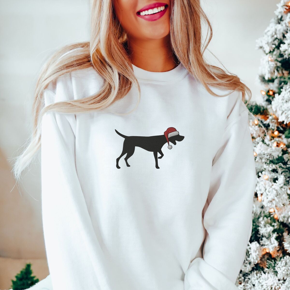 GSP Christmas Sweatshirt - White Woman by a frosted Christmas tree in a White crewneck sweatshirt embroidered with a black German shorthaired pointer silhouette in a red Santa hat