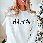 Woman by a frosted Christmas tree in a white crewneck sweatshirt embroidered with four black German shorthaired pointer silhouettes in a striped scarf, a red bow, Christmas lights, a Santa hat and an elf hat under a gold star