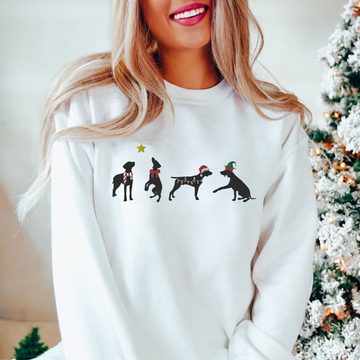 GSP Silhouette Christmas Sweatshirt - worn in white Woman by a frosted Christmas tree in a white crewneck sweatshirt embroidered with four black German shorthaired pointer silhouettes in a striped scarf, a red bow, Christmas lights, a Santa hat and an elf hat under a gold star