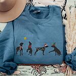 Indigo Blue crewneck sweatshirt laid flat with a tan hat and dried pampas grass, embroidered with four black German shorthaired pointer silhouettes in a striped scarf, a red bow, Christmas lights, a Santa hat and an elf hat under a gold star