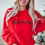 Woman by a Christmas tree in a Red crewneck sweatshirt embroidered with four black German shorthaired pointer silhouettes in a striped scarf, a red bow, Christmas lights, a Santa hat and an elf hat under a gold star
