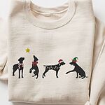 Sand crewneck sweatshirt laid flat on a white background, embroidered with four black German shorthaired pointer silhouettes in a striped scarf, a red bow, Christmas lights, a Santa hat and an elf hat under a gold star