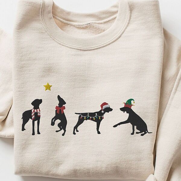 Sand crewneck sweatshirt laid flat on a white background, embroidered with four black German shorthaired pointer silhouettes in a striped scarf, a red bow, Christmas lights, a Santa hat and an elf hat under a gold star