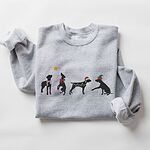Sport Grey crewneck sweatshirt laid flat on a white background, embroidered with four black German shorthaired pointer silhouettes in a striped scarf, a red bow, Christmas lights, a Santa hat and an elf hat under a gold star