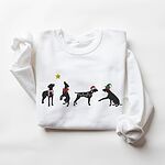 White crewneck sweatshirt laid flat on a white background, embroidered with four black German shorthaired pointer silhouettes in a striped scarf, a red bow, Christmas lights, a Santa hat and an elf hat under a gold star