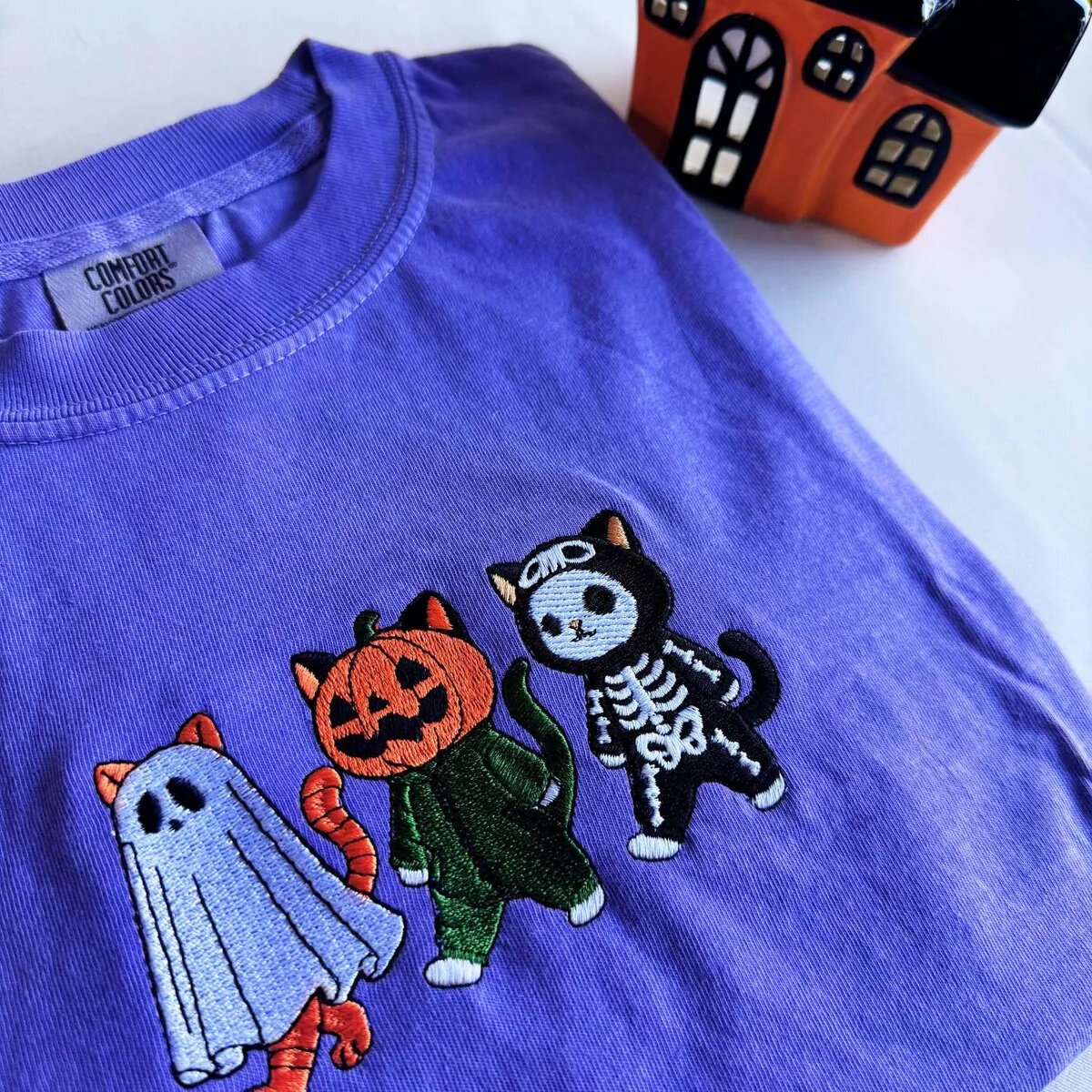Halloween Costume Cats Embroidery Close-up Close-up of the embroidered ghost cat, pumpkin cat and skeleton cat on a violet tee