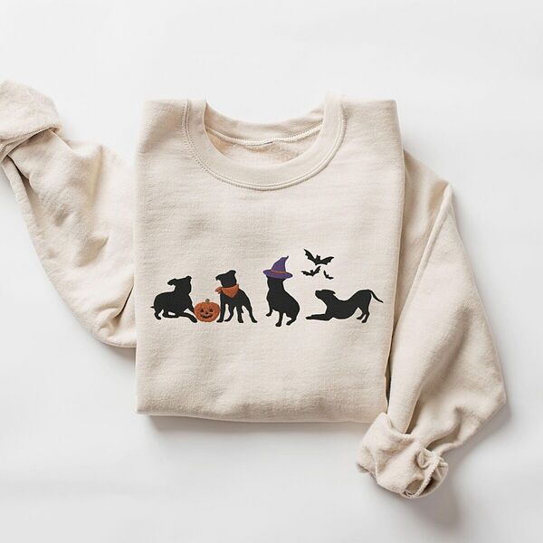 Sand crewneck sweatshirt laid flat on a white background, embroidered with four black pit bull silhouettes with a jack-o'-lantern, an orange bandana, a purple witch hat and bats