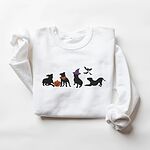White crewneck sweatshirt laid flat on a white background, embroidered with four black pit bull silhouettes with a jack-o'-lantern, an orange bandana, a purple witch hat and bats