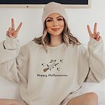 Woman in a beanie making peace signs in a Sand crewneck sweatshirt embroidered with a ghost dachshund on a broom and the words Happy Halloweenie