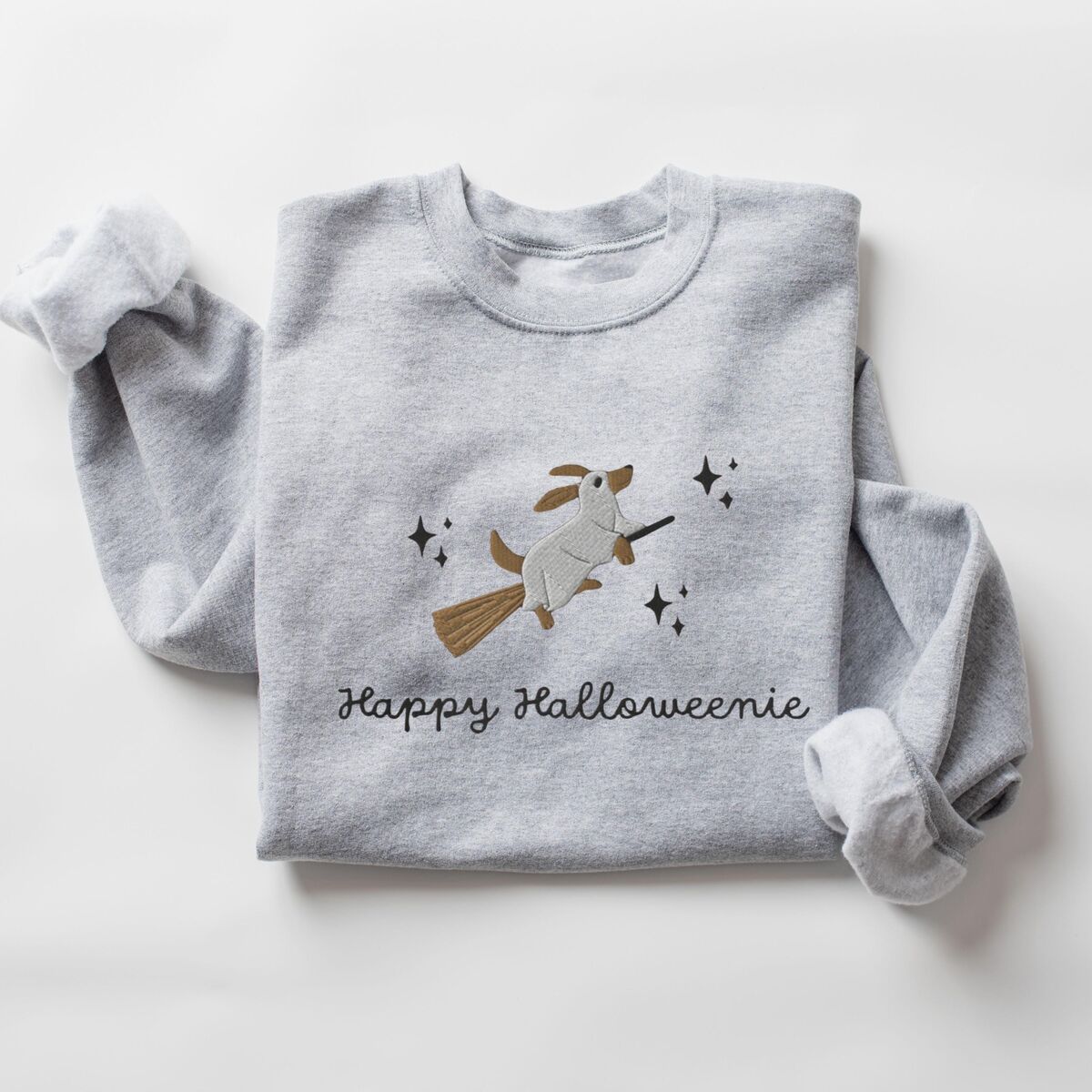 Happy Halloweenie Sweatshirt - Sport Grey Sport Grey crewneck sweatshirt laid flat on white, embroidered with a ghost dachshund riding a broom among black stars above the words Happy Halloweenie