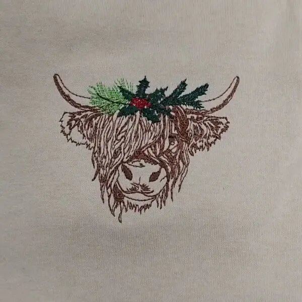 Close-up video of the embroidered highland cow with a holly and pine crown on a Sand sweatshirt