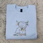 Light Blue Highland cow crewneck with the embroidered floral Highland cow centered on the chest