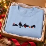 Light blue holiday cat sweatshirt folded in a kraft gift box with a red ribbon and a feather cat toy