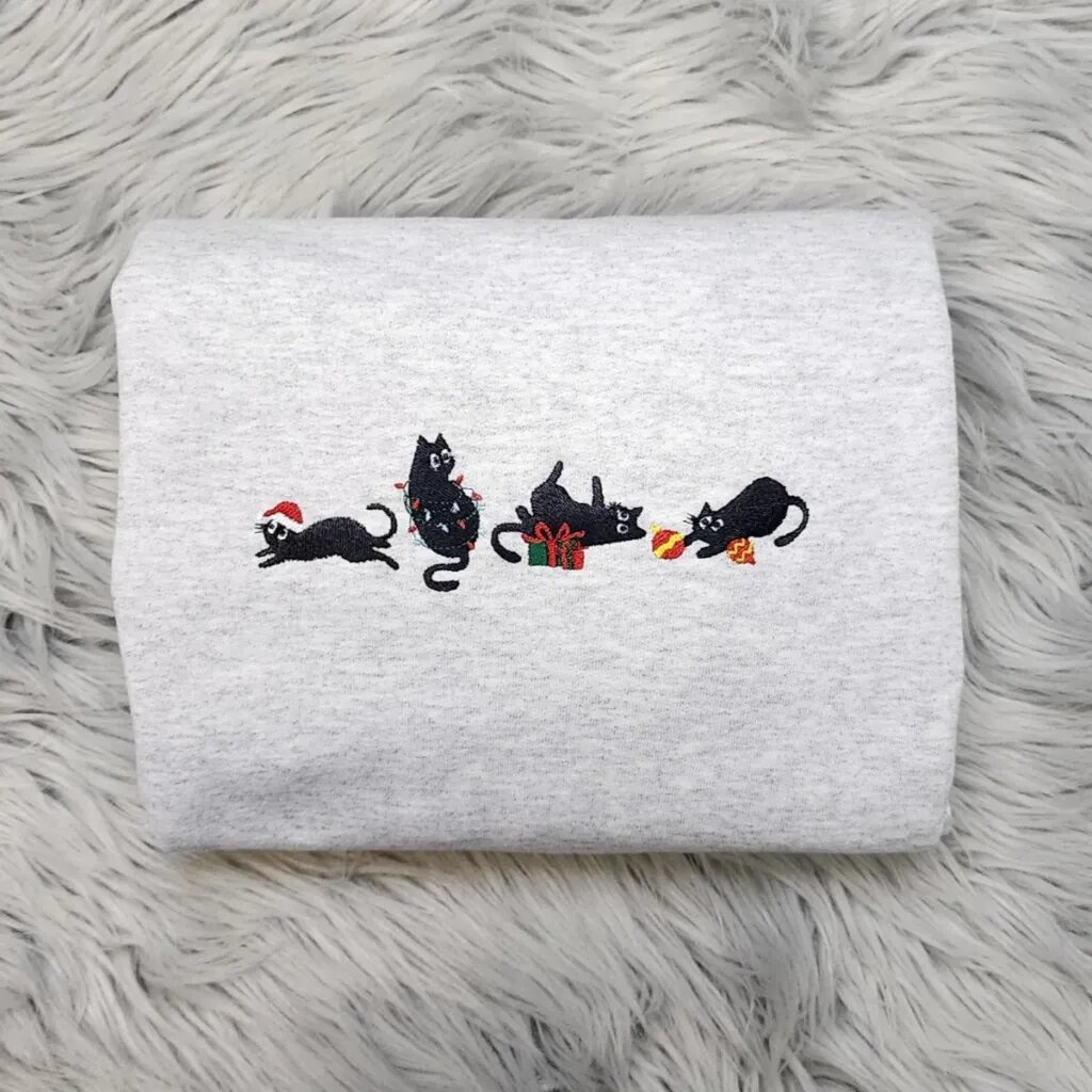 Holiday cat sweatshirt in light heather grey with four embroidered black cats, a Santa hat, Christmas lights, a gift box and ornaments