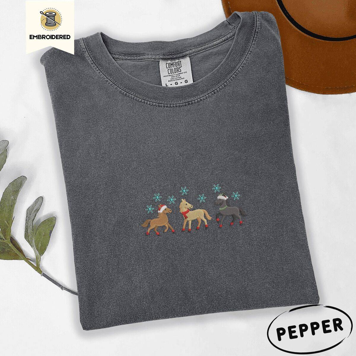 Horse Christmas Shirt – Pepper Pepper Comfort Colors T-shirt embroidered with three horses in Santa hats, a red scarf and red leg wraps trotting under turquoise snowflakes