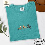 Seafoam Comfort Colors T-shirt embroidered with three horses in Santa hats, a red scarf and red leg wraps trotting under turquoise snowflakes