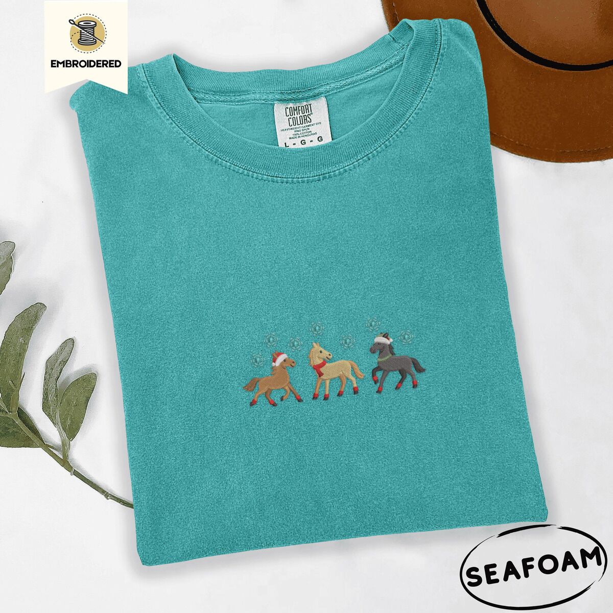 Horse Christmas Shirt – Seafoam Seafoam Comfort Colors T-shirt embroidered with three horses in Santa hats, a red scarf and red leg wraps trotting under turquoise snowflakes