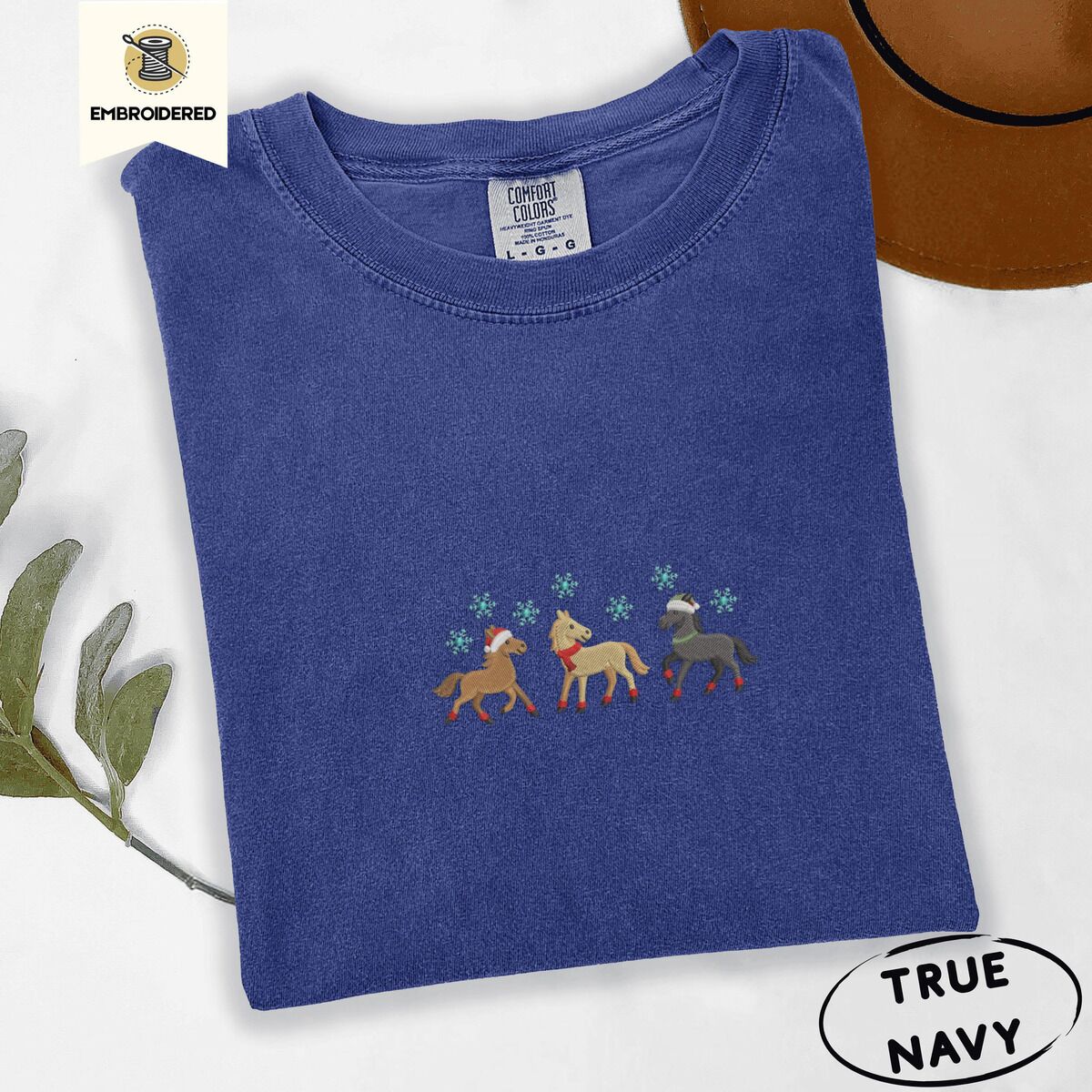 Horse Christmas Shirt – True Navy True Navy Comfort Colors T-shirt embroidered with three horses in Santa hats, a red scarf and red leg wraps trotting under turquoise snowflakes