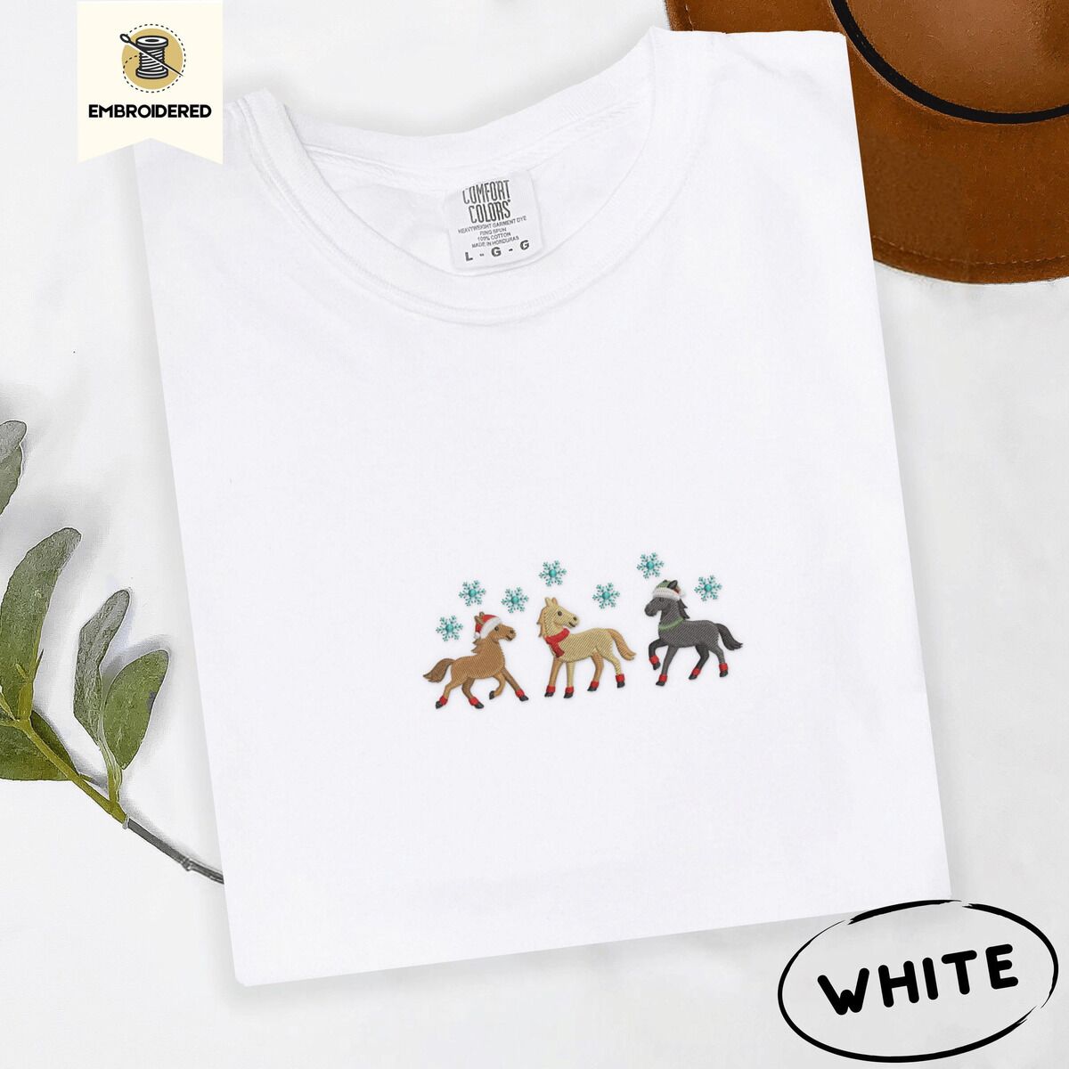 Horse Christmas Shirt – White White Comfort Colors T-shirt embroidered with three horses in Santa hats, a red scarf and red leg wraps trotting under turquoise snowflakes