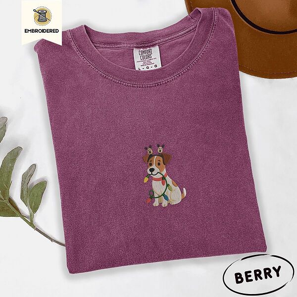 Berry Comfort Colors T-shirt embroidered with a white and tan Jack Russell puppy in a reindeer headband chewing a string of Christmas lights