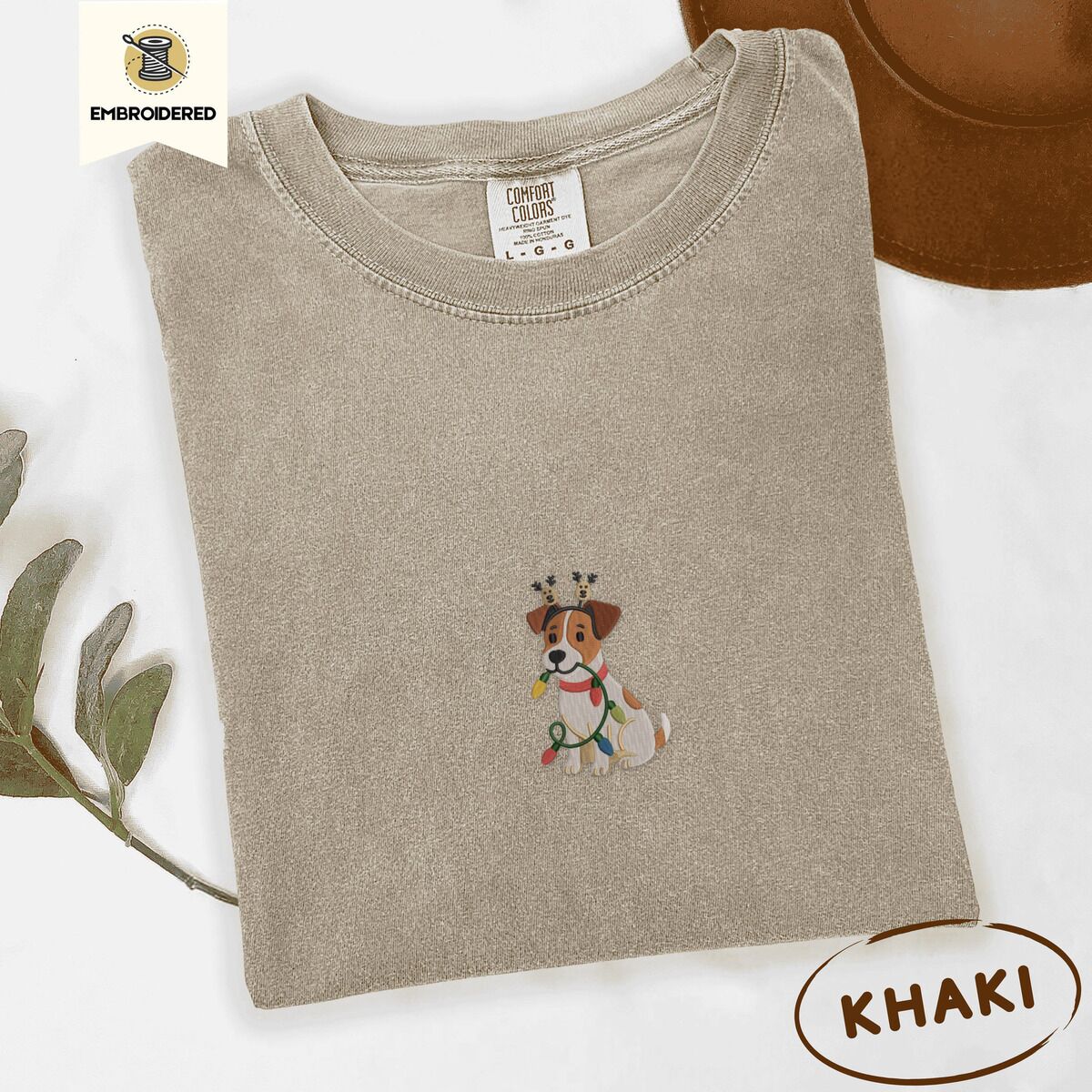 Jack Russell Christmas Lights Shirt – Khaki Khaki Comfort Colors T-shirt embroidered with a white and tan Jack Russell puppy in a reindeer headband chewing a string of Christmas lights