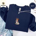 Navy crewneck sweatshirt folded with ripped jeans and a silver chain necklace, embroidered with a white and tan Jack Russell puppy in a reindeer headband chewing a string of Christmas lights