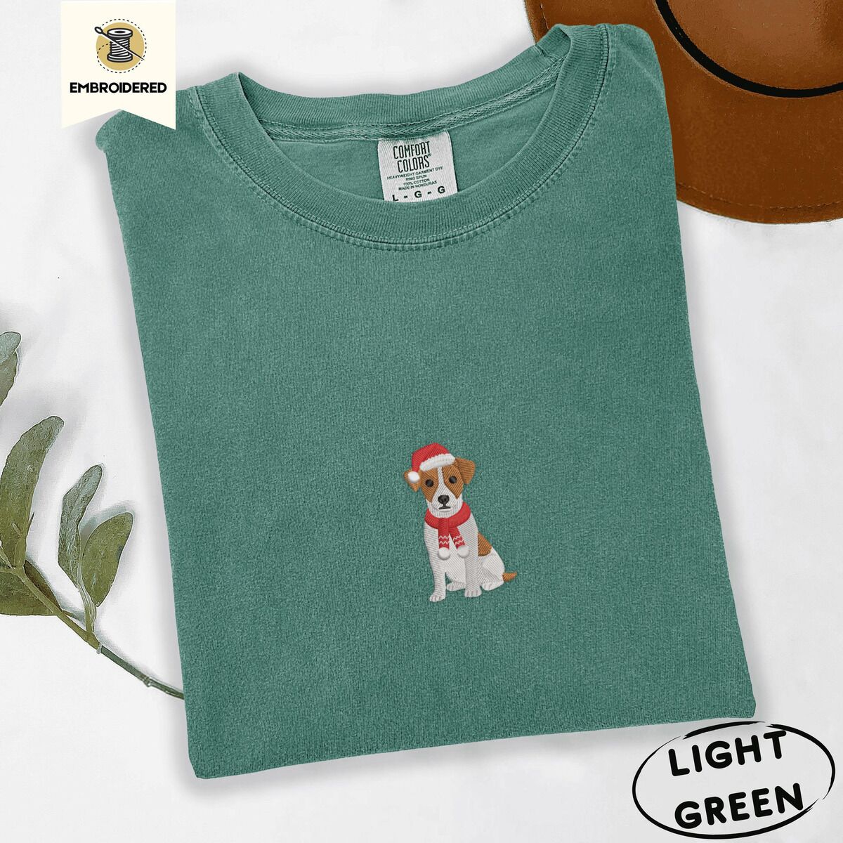 Jack Russell Santa Hat Shirt – Light Green Light Green Comfort Colors T-shirt embroidered with a mini Jack Russell Terrier puppy in a red Santa hat and a knitted red scarf