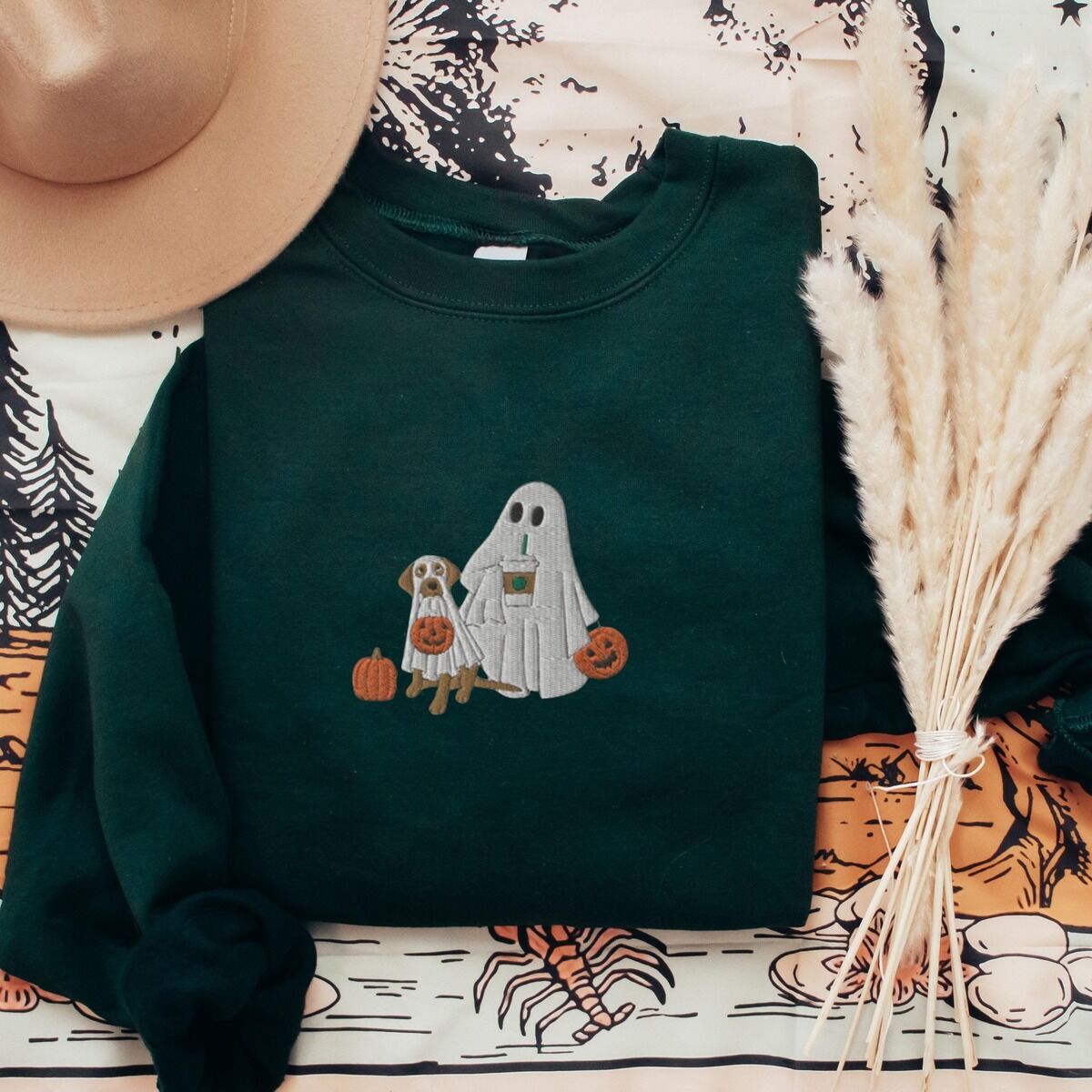 Lab Mom Ghost Sweatshirt – Forest Green Forest Green crewneck sweatshirt laid flat with a brown hat and pampas grass, embroidered with a ghost lab mom holding a coffee cup and a jack-o'-lantern pail beside a tan lab in a ghost sheet with its own pumpkin pail