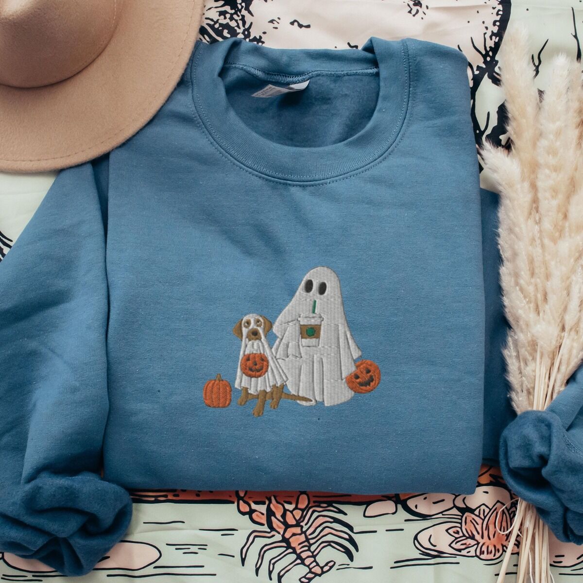 Lab Mom Ghost Sweatshirt – Indigo Blue Indigo Blue crewneck sweatshirt laid flat with a brown hat and pampas grass, embroidered with a ghost lab mom holding a coffee cup and a jack-o'-lantern pail beside a tan lab in a ghost sheet with its own pumpkin pail