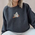 Woman sitting in a dark grey crewneck sweatshirt embroidered with a ghost lab mom holding a coffee cup and a jack-o'-lantern pail beside a tan lab in a ghost sheet with its own pumpkin pail
