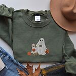 Military Green crewneck sweatshirt laid flat beside jeans, a plaid scarf and autumn leaves, embroidered with a ghost lab mom holding a coffee cup and a jack-o'-lantern pail beside a tan lab in a ghost sheet with its own pumpkin pail