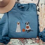 Indigo Blue crewneck sweatshirt laid flat with a brown hat and pampas grass, embroidered with two Labrador ghosts: a light cream lab draped in a white sheet and a black lab in a sheet holding a jack-o'-lantern, with a pumpkin between them
