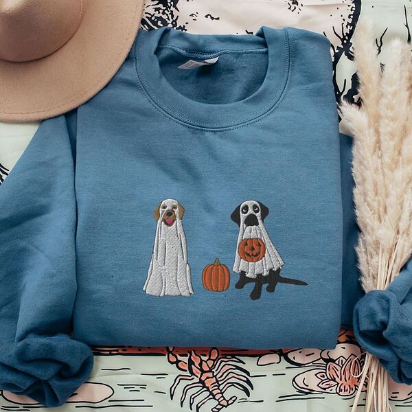 Indigo Blue crewneck sweatshirt laid flat with a brown hat and pampas grass, embroidered with two Labrador ghosts: a light cream lab draped in a white sheet and a black lab in a sheet holding a jack-o'-lantern, with a pumpkin between them