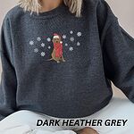 Woman sitting in a Dark Heather crewneck sweatshirt embroidered with a sitting Labrador in a red Santa hat and a fringed red scarf, framed by snowflakes