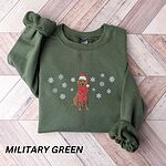 Military Green crewneck sweatshirt laid flat on a chevron wood floor, embroidered with a sitting Labrador in a red Santa hat and a fringed red scarf, framed by snowflakes