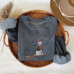 Dark Heather crewneck sweatshirt laid flat in a woven basket with a brown hat, embroidered with a pale cream lab in a purple and orange witch hat and a jack-o'-lantern cape, riding a broomstick with a trail of bats