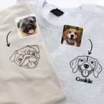 Sand and grey crewnecks with an embroidered line art pug face in brown thread and a beagle face with the name Cookie in black thread