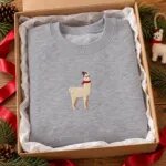 Sport grey llama Christmas sweatshirt folded in a kraft gift box with a red ribbon and a felt llama ornament