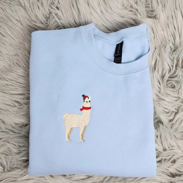 Llama Christmas sweatshirt in light blue with a small embroidered cream llama wearing a red pom-pom beanie and a red scarf