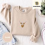 Sand crewneck sweatshirt folded with denim shorts, white sneakers and a potted plant, embroidered with a longhorn steer head with cream and copper patches and long curved horns
