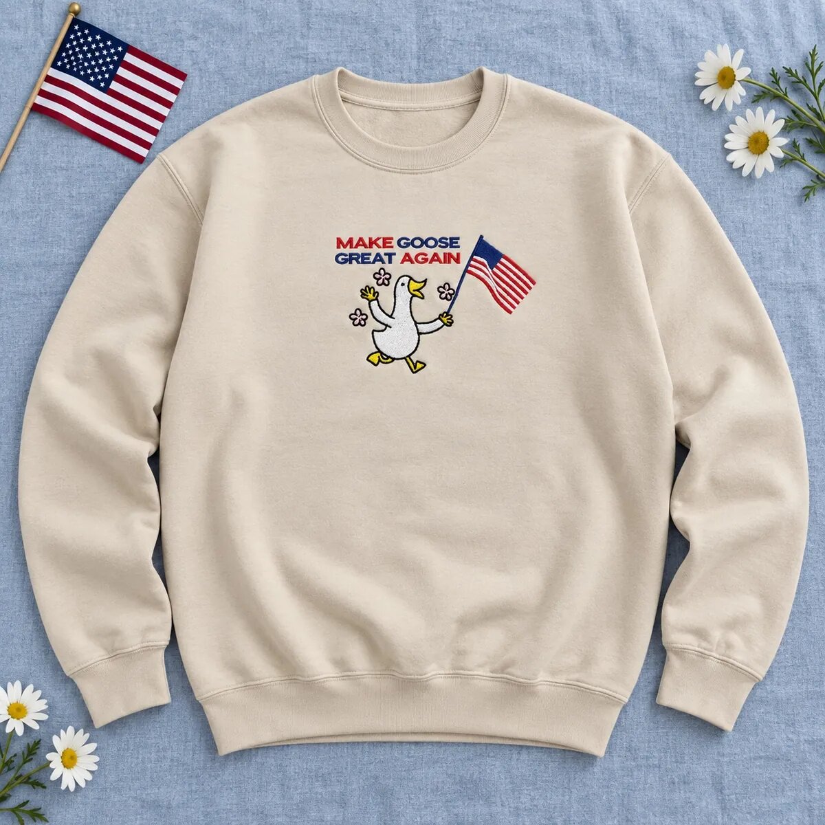 Make Goose Great Again Crewneck – Sand Sand Make Goose Great Again crewneck laid flat with an embroidered goose waving an American flag